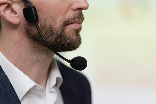 Close-up of lower part of face of young serious businessman with microphone under his chin against white background