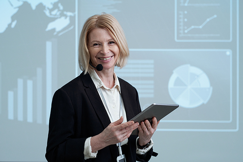 Successful mature female entrepreneur with tablet standing against interactive board while making report at conference