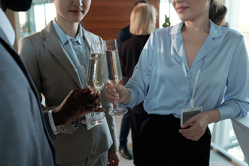 Three young successful brokers in formalwear clinking with flutes of champagne at buffet in restaurant of business center