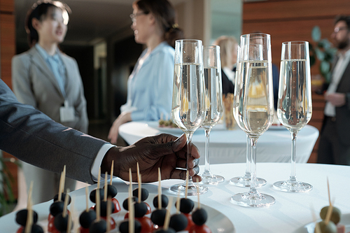 Hand of young African American businessman taking flute of champagne from served table during buffet in restaurant after conference