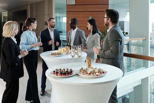 Group of intercultural business people in formalwear looking at man with flute of champagne pronouncing toast for successful project