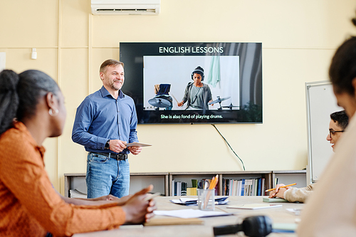 Mature Caucasian teacher working with group of multi-ethnic migrants teaching them English language