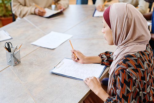 High angle shot of young woman in hijab attending classes for immigrants doing English language grammar test