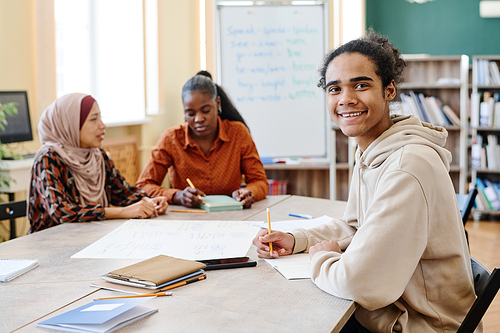 Young Black man sitting at table enjoying learning English language at school for immigrants smiling at camera