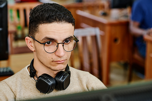 High angle close-up of serious Middle Eastern student wearing headphones working on computer in library