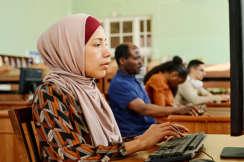 Young adult Middle Eastern woman wearing hijab working on computer in university library