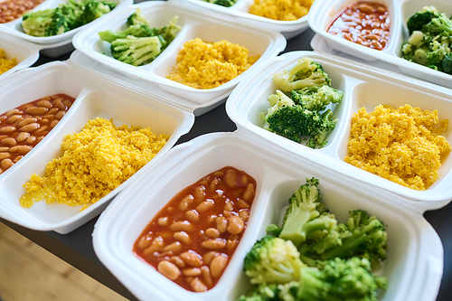 Part of table served with steamed broccoli, kasha and boiled beans in white plastic containers prepared for homeless people