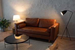 Spacious living room of luxurious apartment with leather sofa standing in center between two lamps and round table in front