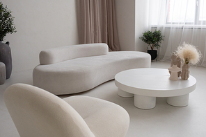 Large living-room with white comfortable sofa and armchair and round table with group of handmade vases with dry wildflowers