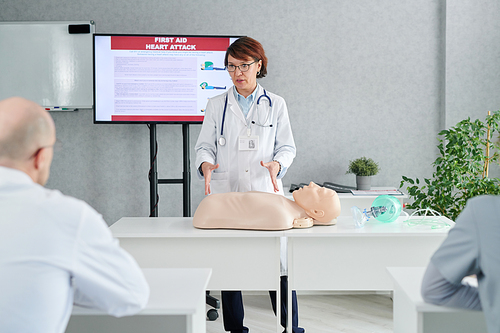 Female mature doctor in white coat showing how to doheart massage to students during medical training at class