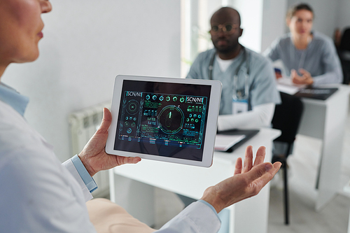 Close-up of mature lecturer holding digital tablet with graphs in his hands and talking to students during medical training