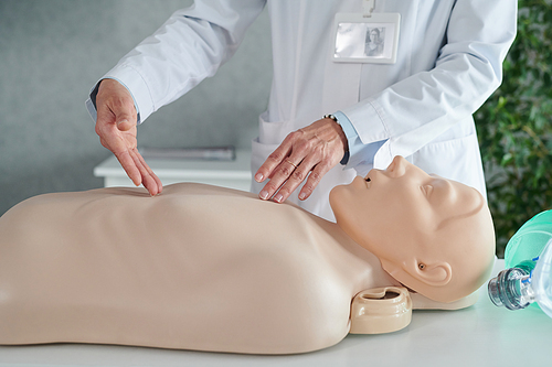 Close-up of physician in white coat demonstrating chest compression on mannequin at table during medical seminar