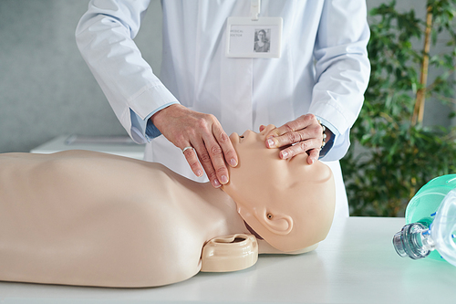 Close-up of female doctor in white coat showing how to make artificial respiration on mannequin at seminar