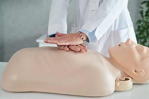 Close-up of female doctor in white coat practicing artificial breathing on mannequin at table