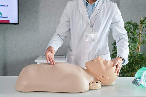 Close-up of medical instructor in white coat standing at table and demonstrating CPR on mannequin during medical training