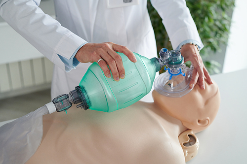 Close-up of female doctor in white coat learning to do artificial respiration with oxygen mask on mannequin