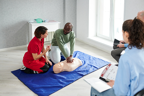 Female doctor explaining to man how to make chest compression during medical training on mannequin