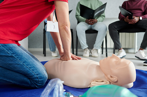 Close-up of paramedic demonstrating cardiopulmonary resuscitation on a mannequin on floor to medical students