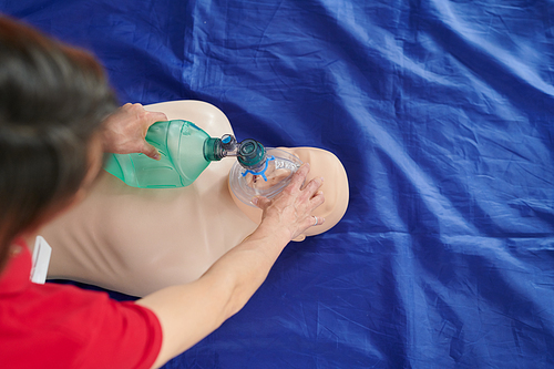 High angle view of paramedic demonstrating reanimation with artificial ventilation using oxygen mask on floor during training