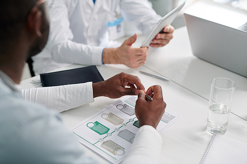 Close-up of group of business people sitting at table with documents and discussing work during meeting