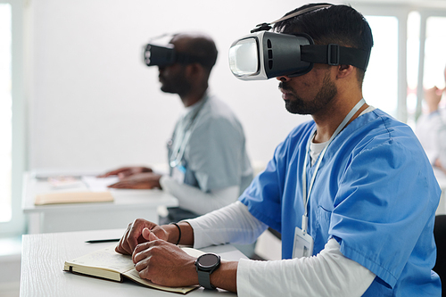 Medical students sitting at desk with VR goggles and getting knowledge during virtual reality