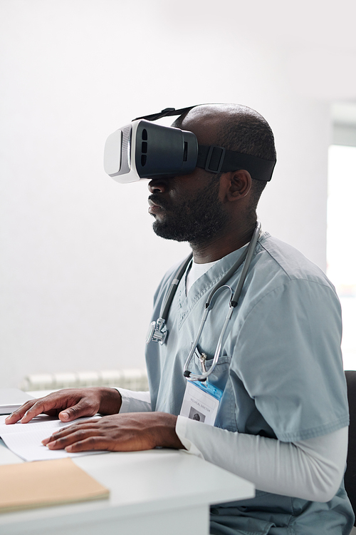 African medical student in uniform using VR glasses while sitting at desk at conference