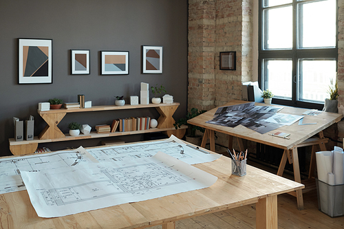 Group of blueprints with architectural sketches on large wooden table in contemporary office or workshop