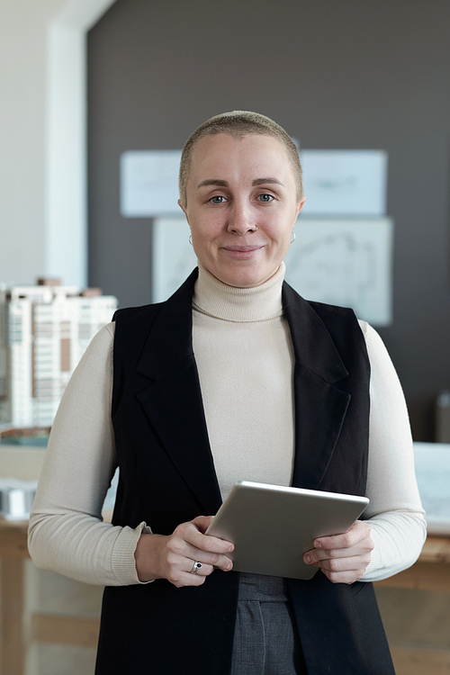 Happy female architect with digital tablet looking at you while standing in front of camera in office environment