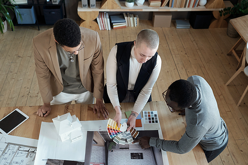 Two designers of interior showing color palette to African male client and consulting him in office or architectural bureau