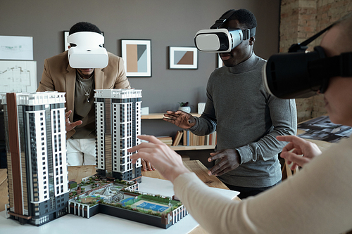 Group of architects in vr headsets standing around table with house layout during presentation of new block of flats