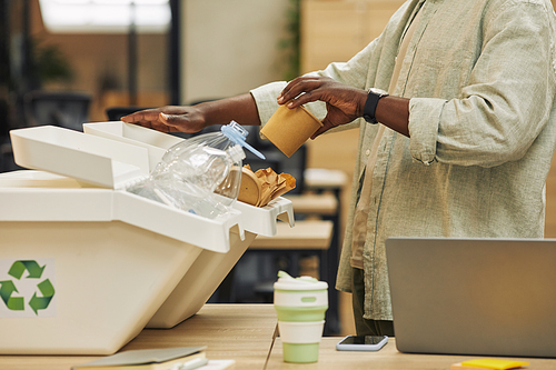 Cropped portrait of unrecognizable African-American man putting paper cup into waste sorting bin in office, copy space