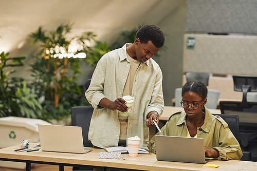 Portrait of two African-American people working in modern open space office, focus on young man instructing colleague and pointing at laptop screen , copy space