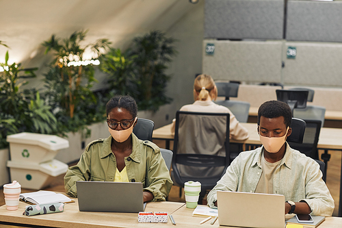 Portrait of two young African-American people wearing masks while working at desk in post pandemic office, copy space