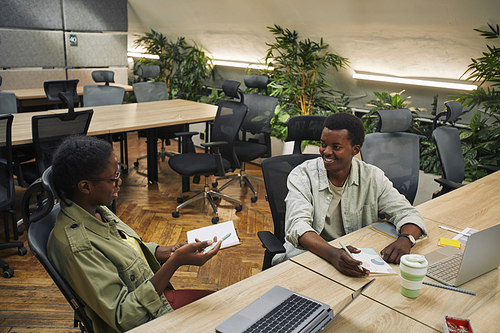High angle portrait of two young African-American people discussing project and smiling while working in modern office interior, copy space