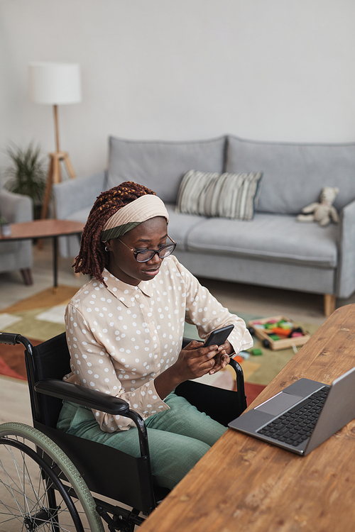Vertical high angle portrait of young African-American woman using wheelchair while working from home with childrens toys in background