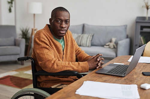 Portrait of adult African-American man using wheelchair while working from home and looking at camera, copy space