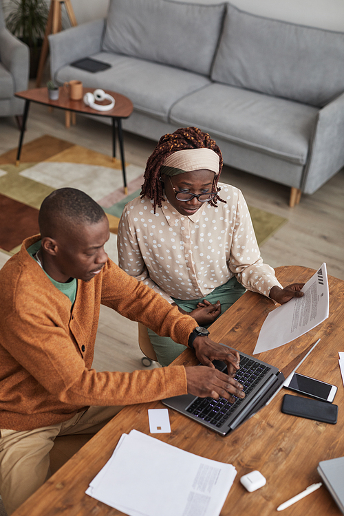 Vertical high angle portrait of young African-American couple working from home together and using laptop, copy space