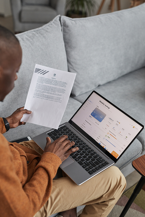 Vertical high angle view at African-American man using laptop with online banking service on screen, copy space