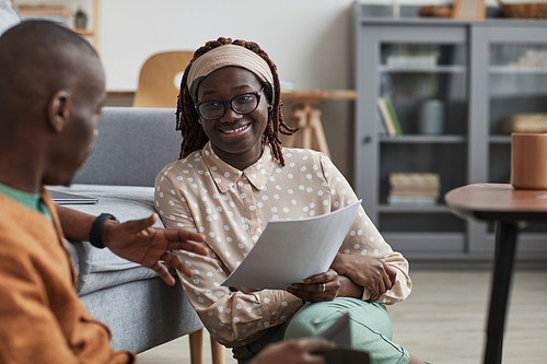 Portrait of modern African-American couple working from home together, focus on smiling young woman holding document while sitting on floor, copy space