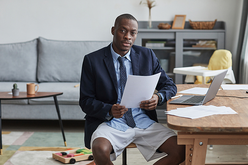 Portrait of African-American man wearing jacket and shorts while working from home and looking at camera, copy space