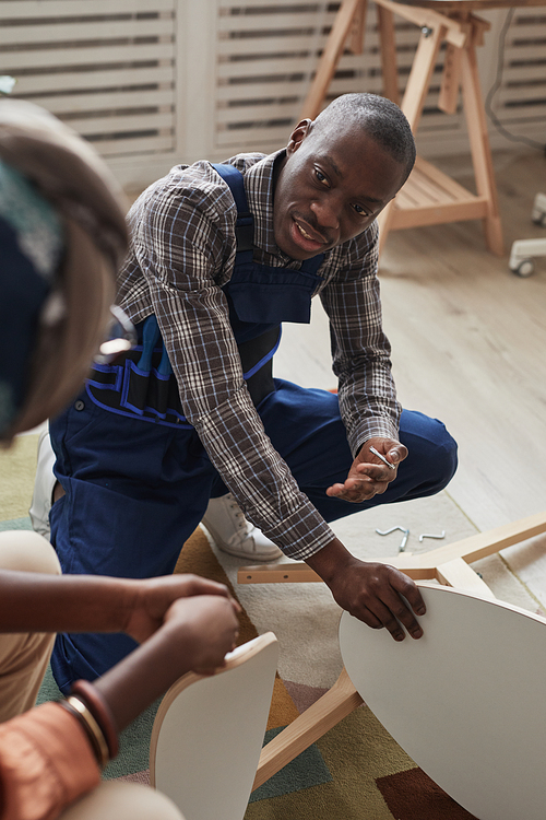 Vertical high angle portrait of African-American handyman helping young woman repair table and chairs