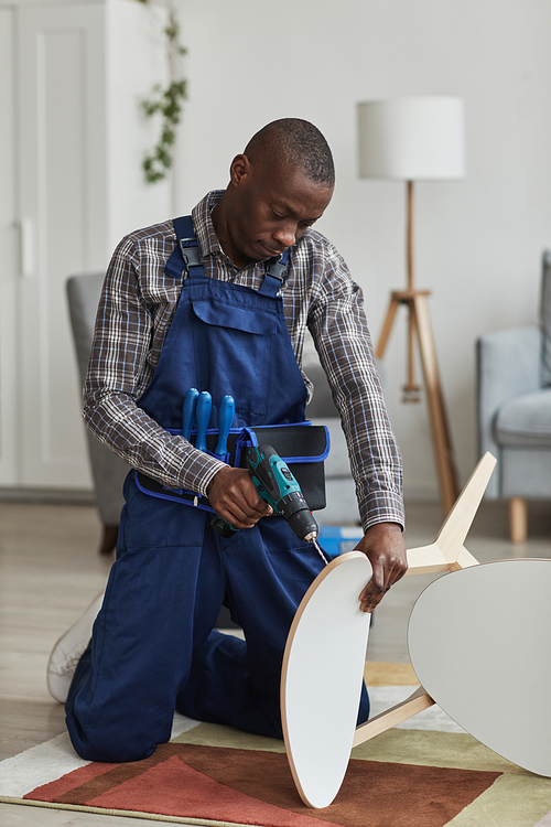 Vertical full length portrait of African-American handyman assembling furniture in home interior