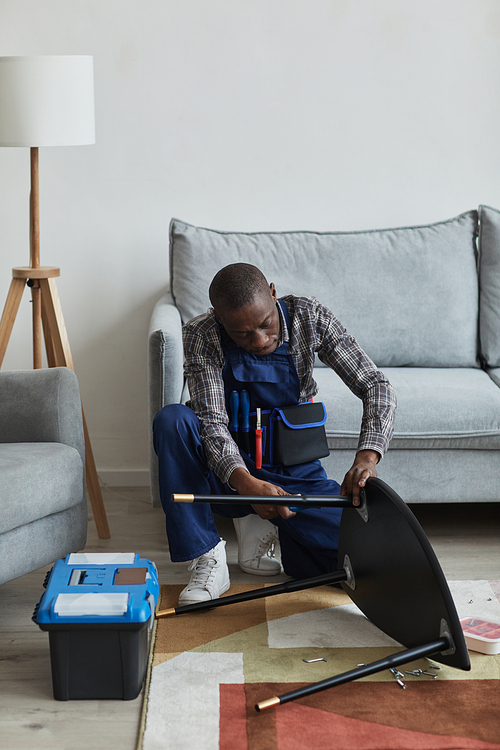 Vertical full length portrait of African-American handyman assembling furniture in home interior, service and assistance concept