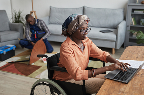 Portrait of modern African-American woman using wheelchair and working from home with handyman assembling furniture in background, service and assistance concept, copy space