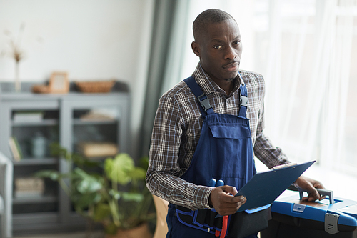 Waist up portrait of African-American handyman looking at camera while standing with toolbox in home interior, copy space