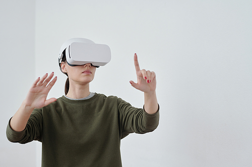 Young contemporary female employee in vr headset pointing at object in virtual reality while making presentation of new project
