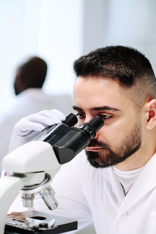 Young male worker of contemporary scientific laboratory using microscope during research of new virus or bacteria