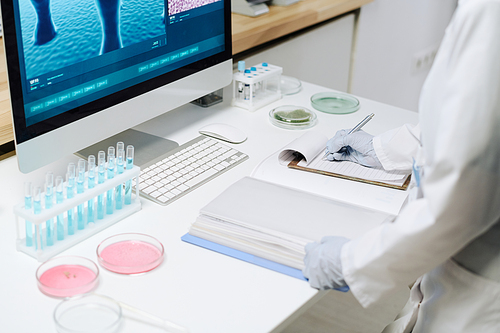 Workplace of biotechnologist with flasks with blue liquid, petri dishes containing pink substance and computer with covid macro image