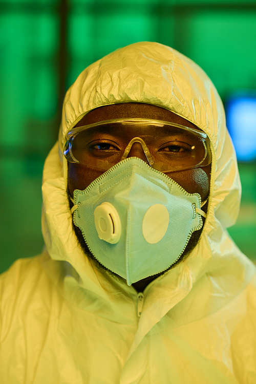 Contemporary black man in white protective coveralls, respirator and eyeglasses looking at camera during work in clinical laboratory