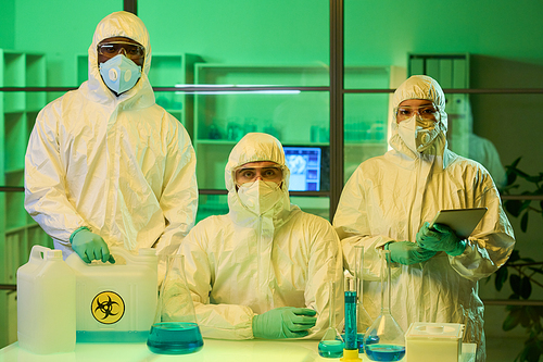 Group of young intercultural scientists or lab workers in protective coveralls, gloves, eyeglasses and respirators looking at camera